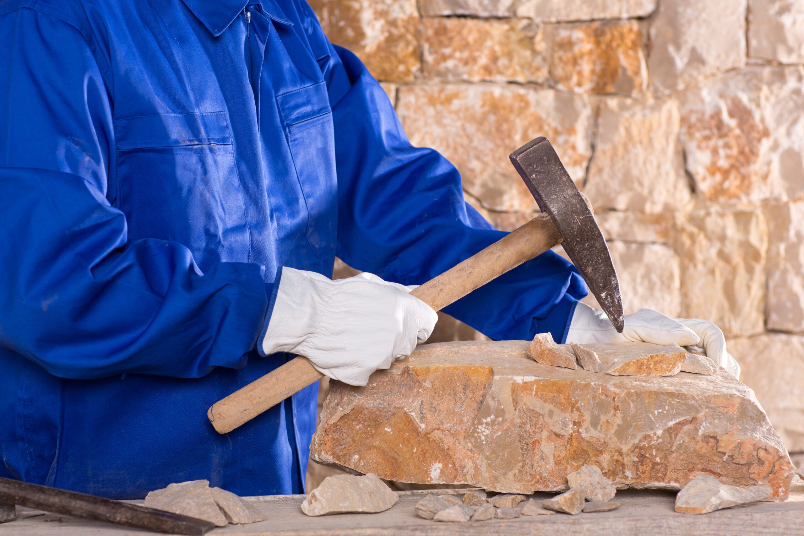Masonry mason stonecutter man with hammer working on stone wall construction